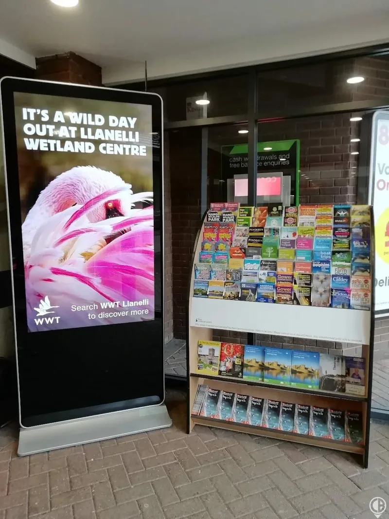A leaflet stand beside a digital screen at a visitor attraction