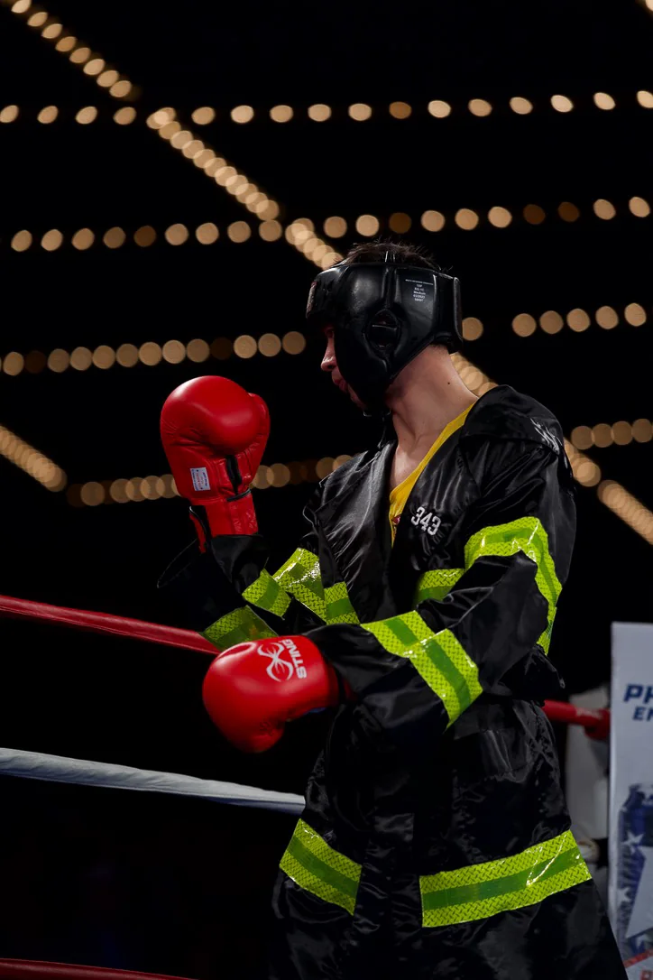 A firefighter boxer in fire kit and red gloves in the ring at Battle of the Badges