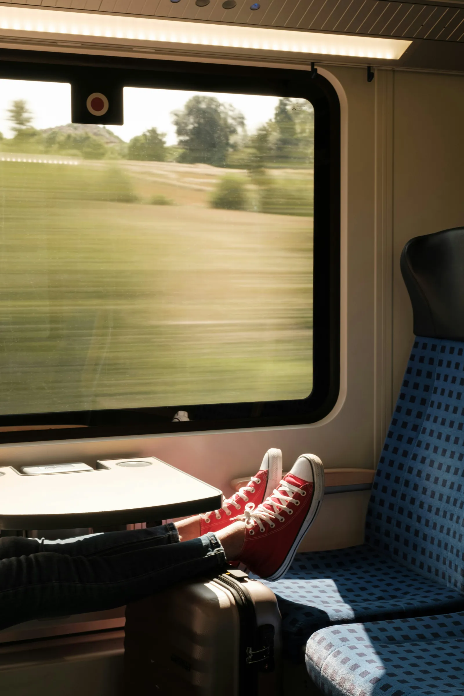 A traveller in red trainers by a train window, the countryside rushing past